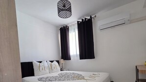 Een slaapkamer met een bed, zwarte gordijnen, een plafondlamp, een airconditioning en een kleine tafel.