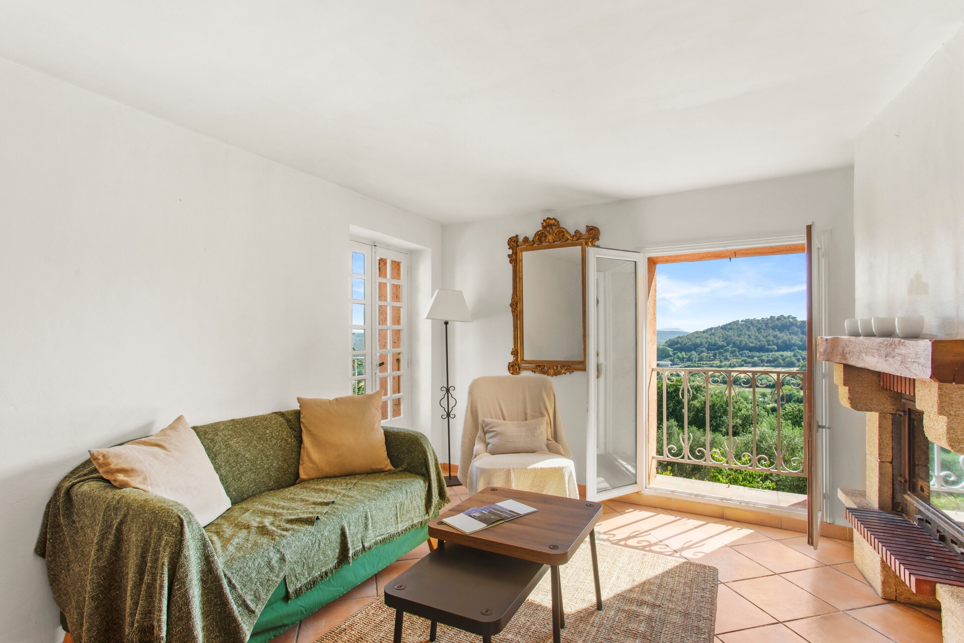 Una habitación con sofá, sillón, mesa, espejo y balcón con vistas.
