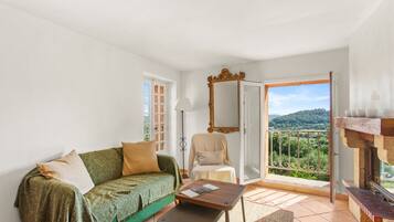 Una habitación con sofá, sillón, mesa, espejo y balcón con vistas.