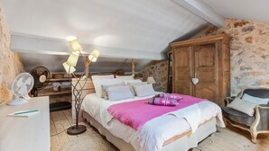 Une chambre à coucher comprenant un lit, une table de chevet, une lampe, un ventilateur et une armoire.