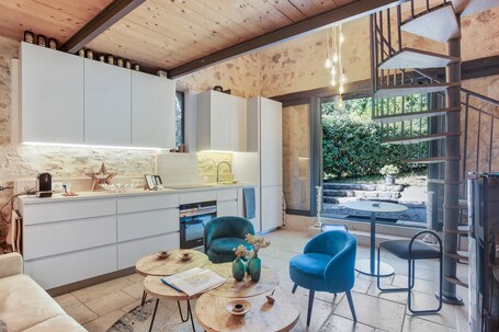 Una cucina moderna con mobili bianchi, una zona pranzo con tavolo rotondo e sedie blu, e una scala che conduce a uno spazio esterno.. La Petite Maison D'emmanuelle