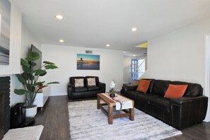 A living room with a black leather sofa, a wooden coffee table, a large potted plant, and a painting on the wall. - Modern 4-bedroom house in charming Huntington Beach with spacious backyard (Huntington Beach)