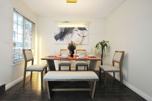 A dining area with a table set for four, a bench, and a large abstract painting above the table. - Modern 4-bedroom house in charming Huntington Beach with spacious backyard (Huntington Beach)