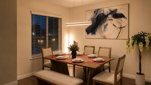 A dining room with a wooden table set for four, a bench, and a large abstract painting on the wall. - Modern 4-bedroom house in charming Huntington Beach with spacious backyard (Huntington Beach)