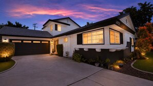 A two-story house with a garage, a well-lit driveway, and a landscaped front yard. - Modern 4-bedroom house in charming Huntington Beach with spacious backyard (Huntington Beach)