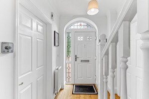 A hallway with white doors, a radiator, a welcome mat, and a staircase with white balusters. - The Wiltshire •  Detached 5BR House • Driveway Parking • Work Space • Smart TVs • By Yoko Property (Milton Keynes)