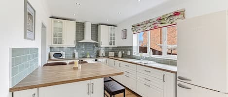A modern kitchen with white cabinets, a wooden countertop, and a window with a view of the outside.