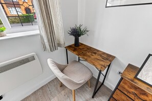 A corner room with a window, a radiator, a chair, a small wooden table, and a plant. - The Wiltshire •  Detached 5BR House • Driveway Parking • Work Space • Smart TVs • By Yoko Property (Milton Keynes)