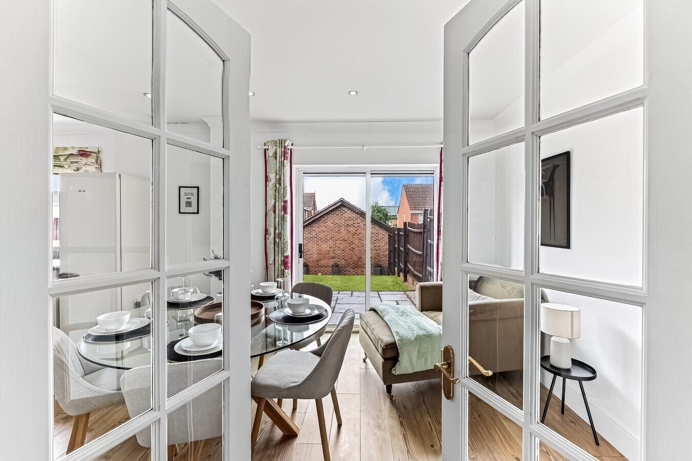 An open-plan living area with a dining table set for four, a sofa, and a lamp.