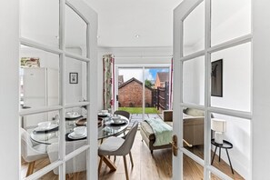An open-plan living area with a dining table set for four, a sofa, and a lamp. - The Wiltshire •  Detached 5BR House • Driveway Parking • Work Space • Smart TVs • By Yoko Property (Milton Keynes)