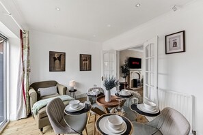A modern living room with a dining area, a fireplace, and a television displaying 'NETFLIX'. - The Wiltshire •  Detached 5BR House • Driveway Parking • Work Space • Smart TVs • By Yoko Property (Milton Keynes)