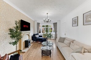 Een woonkamer met een open haard, een televisie waarop Netflix afspeelt, een kroonluchter en een bank.