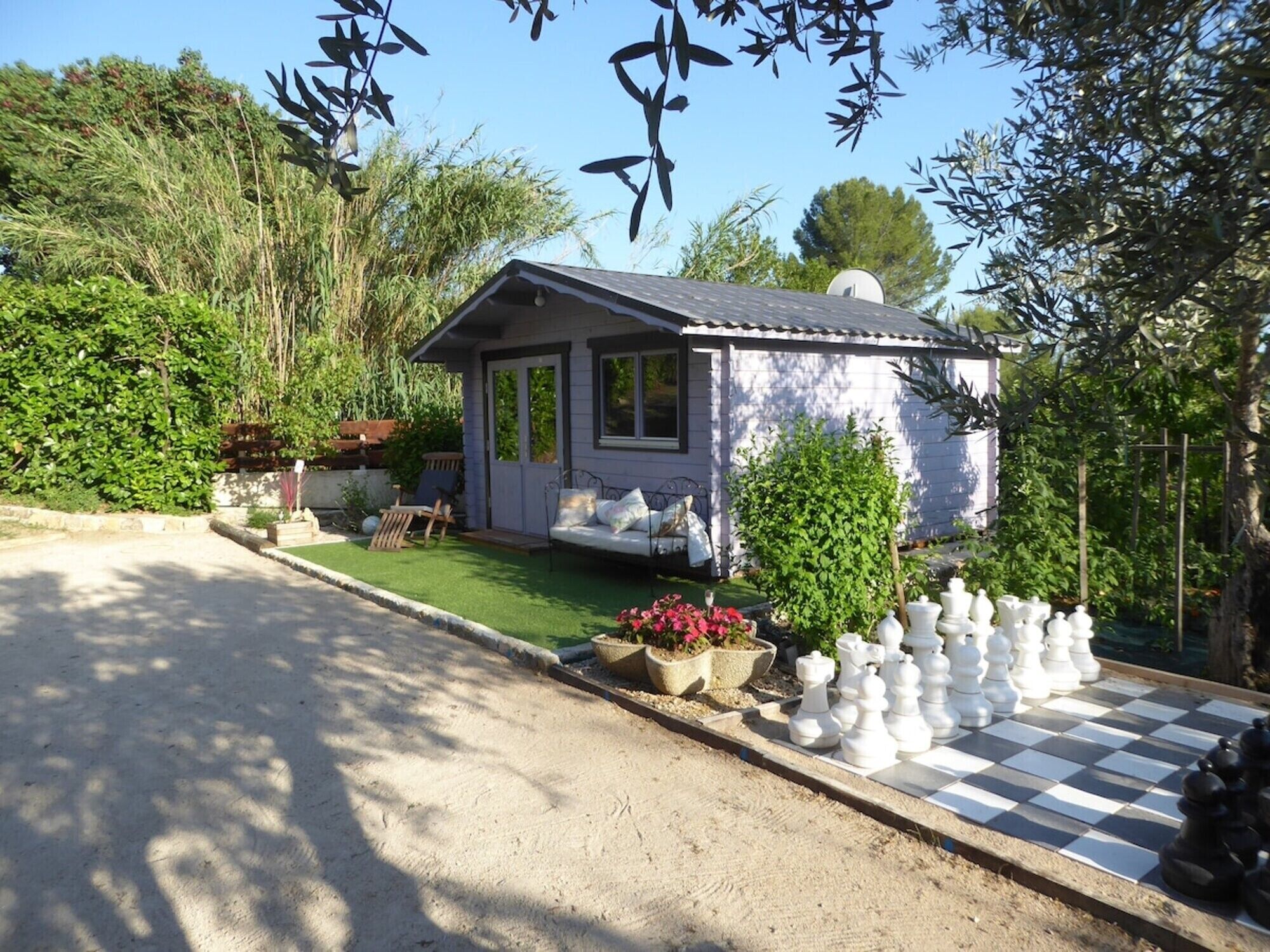 A small house with a porch, a garden with potted plants, and a chessboard.