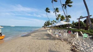 Een strand met palmbomen, een boot en ligbedden onder parasols.