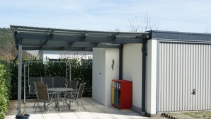 Un patio coperto con tavolo e sedie, un piccolo armadietto rosso e un edificio con rivestimento verticale.