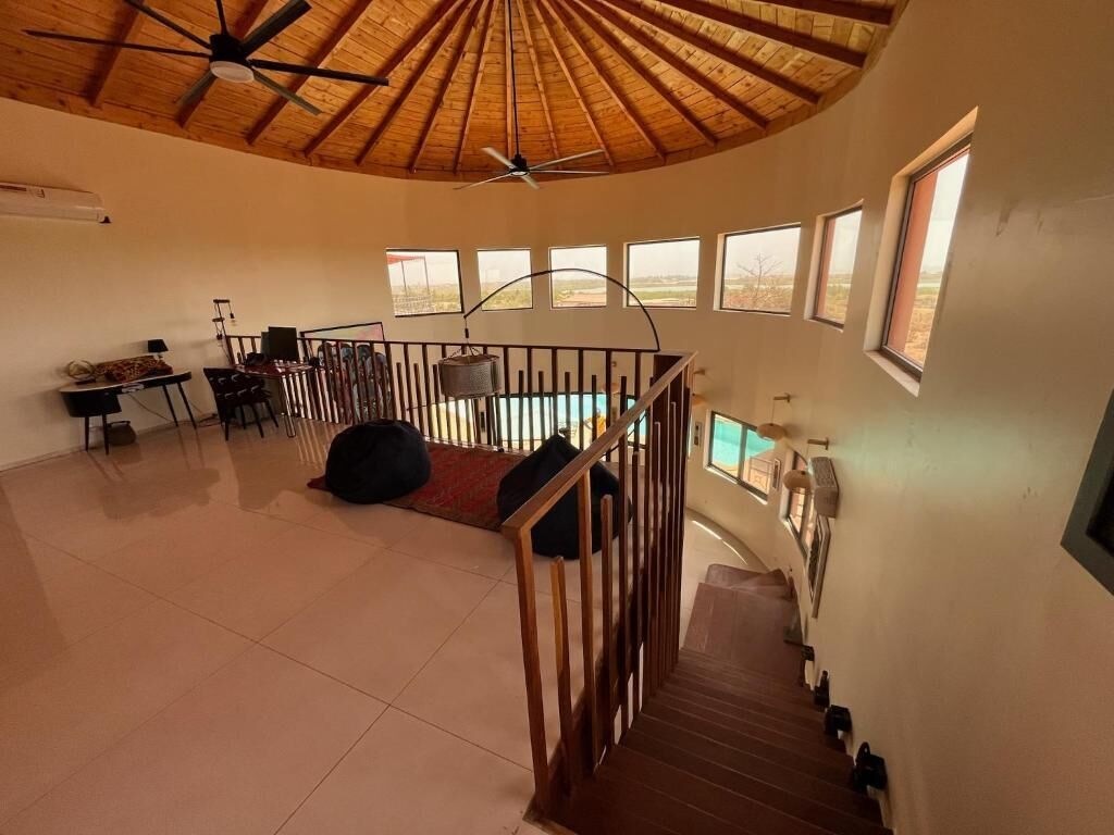 A spacious room with a high ceiling, a staircase, and multiple windows offering views of the outdoors.