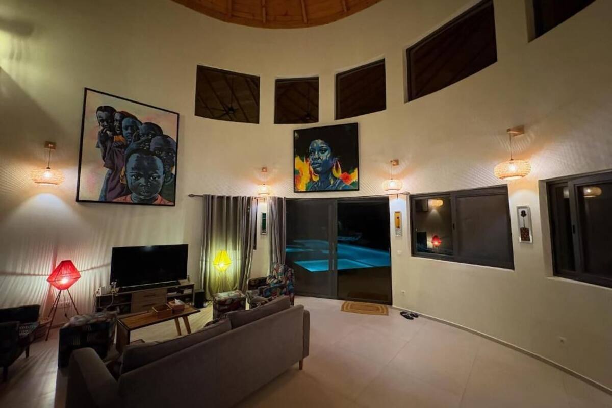 A spacious living area with a large flat-screen TV, comfortable seating, artwork on the walls, and a view of the pool.