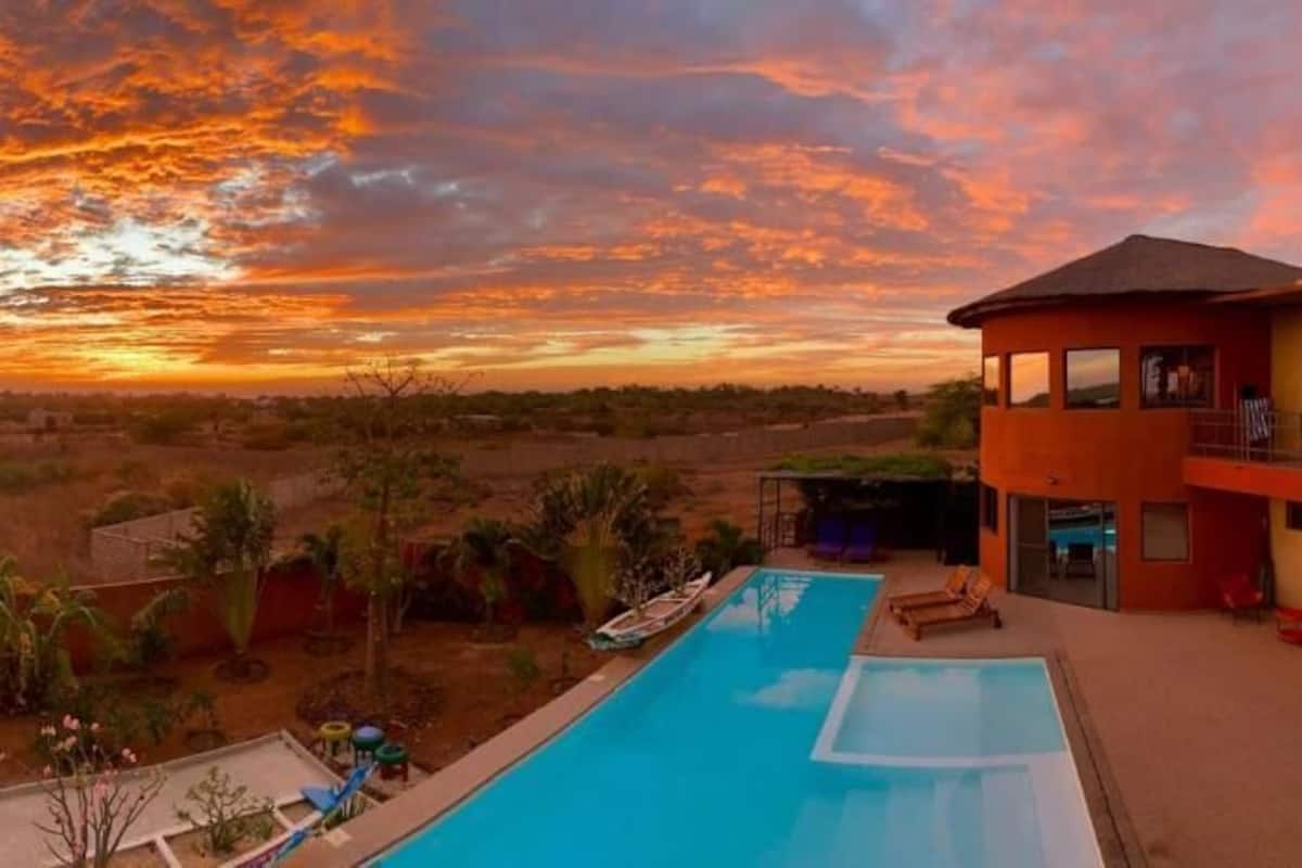 A pool with a sunset view, a two-story building, and surrounding vegetation.