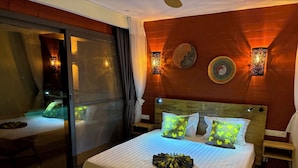 A hotel room with a bed, a nightstand, a wall-mounted lamp, and a sliding glass door. - Lodge Terre et Mer (Guereo)