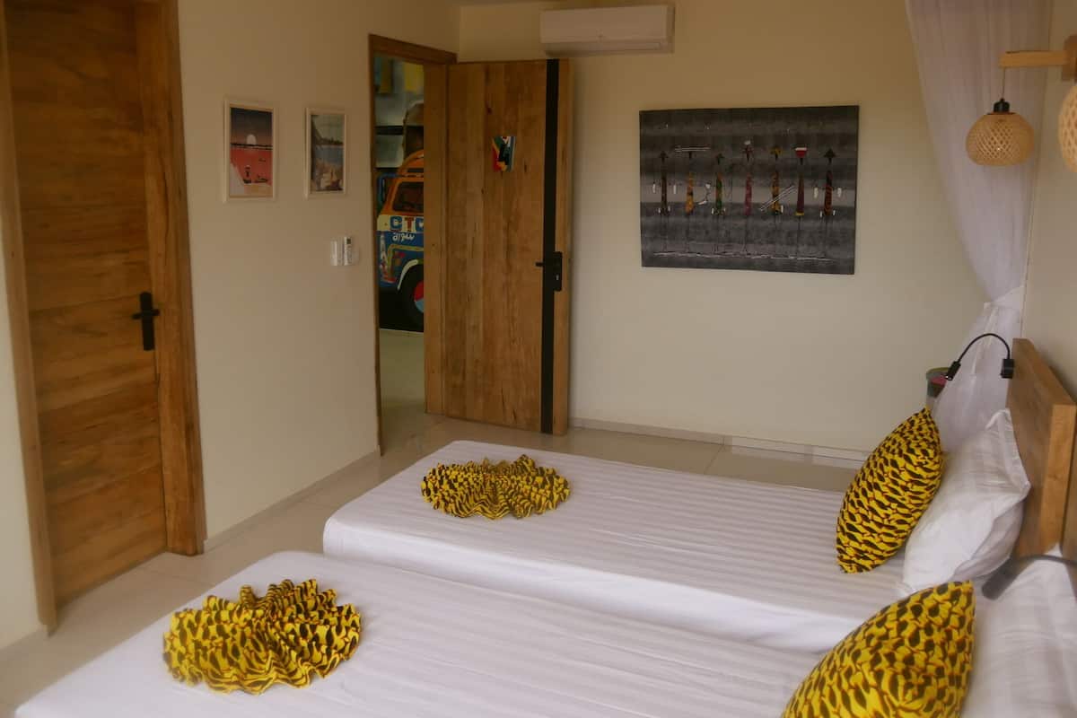 A room with two beds, a wooden door, a wall-mounted air conditioner, and a painting.