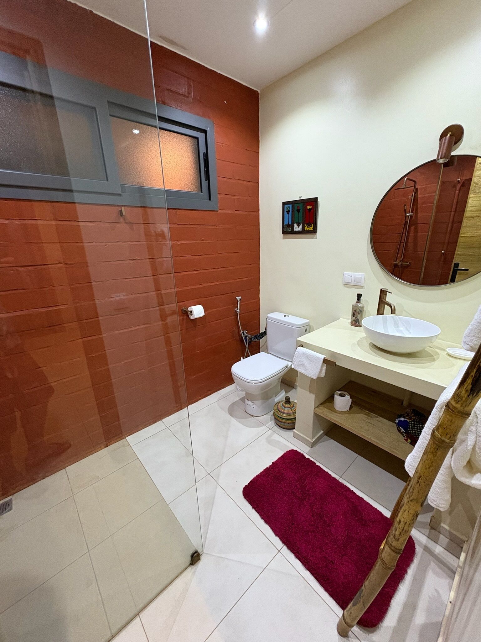 Une salle de bain avec une douche à parois de verre, des toilettes blanches, un lavabo avec un miroir et un tapis de bain rouge.