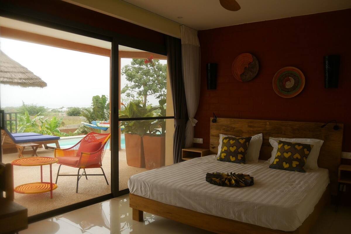 A hotel room with a bed, a small table, a chair, and a view of the outdoors.