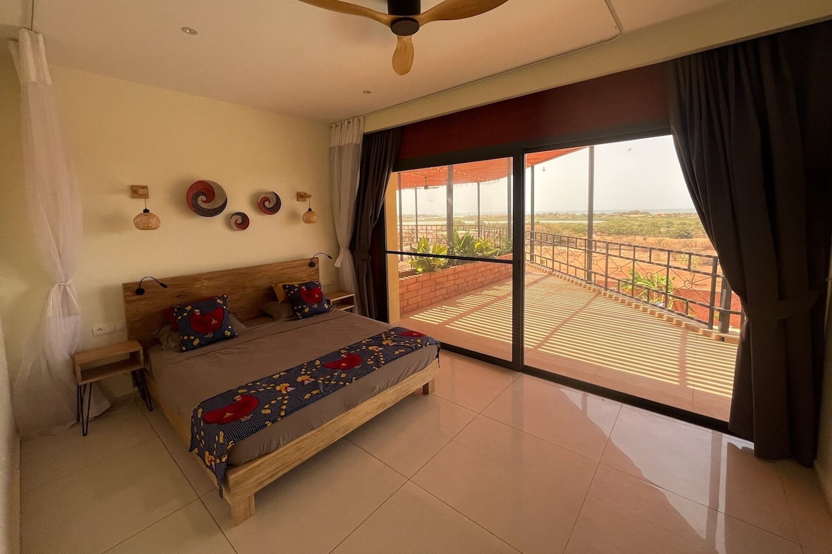 A bedroom with a bed, a ceiling fan, a view of the outdoors, and a balcony.