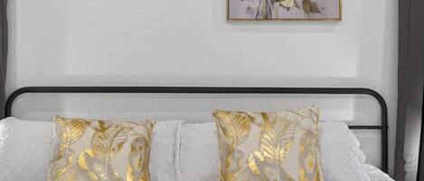 A bed with a dark blue blanket, white pillows with gold leaf patterns, and two floral paintings on the wall.