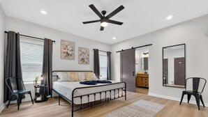 A bedroom with a bed, a ceiling fan, a nightstand, a chair, a dresser, a mirror, and a door. - Lovely and Stylish Modern Home Near Downtown (San Antonio)