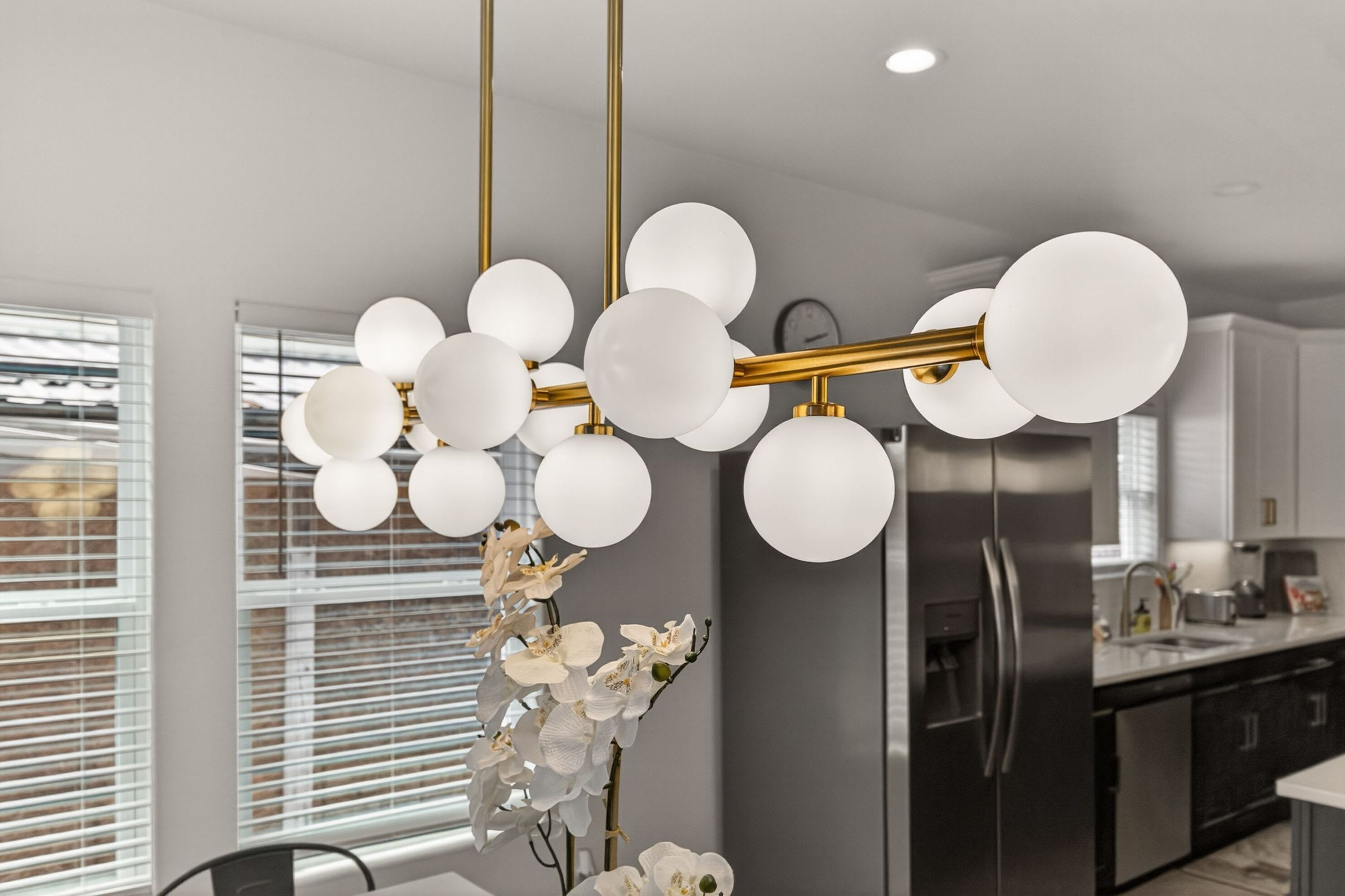 A modern kitchen with a central light fixture, stainless steel appliances, and white cabinetry.