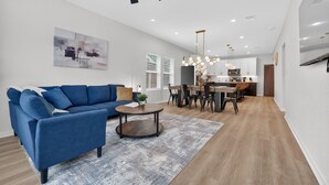 A modern living room with a blue sofa, a round coffee table, and a dining area with a wooden table and chairs. - Lovely and Stylish Modern Home Near Downtown (San Antonio)