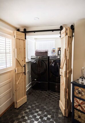 A laundry room with two black washing machines, a stack of folded towels, and a Tide detergent bottle. - McDonald Manor/Walk To DT Mt Dora/Boat Parking (Mount Dora)