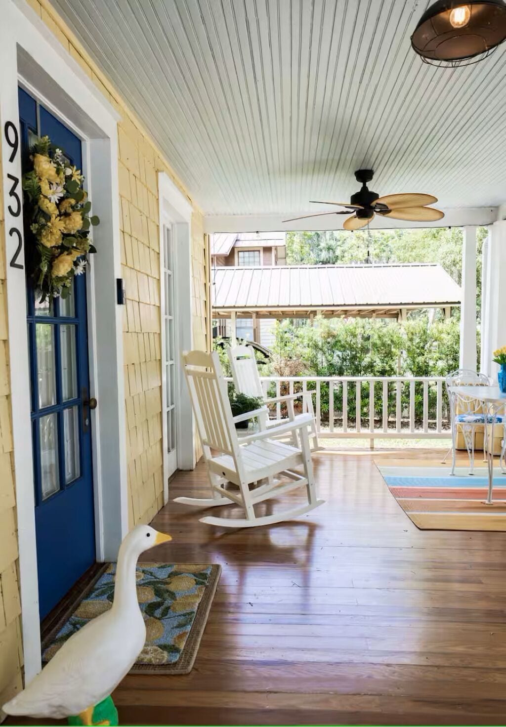 Eine Veranda mit einem weißen Schaukelstuhl, einer weißen Schwaneinrichtung und einer blauen Tür mit der Nummer 932.