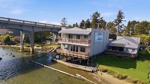 A waterfront building with a dock, a bridge in the background, and a grassy area.