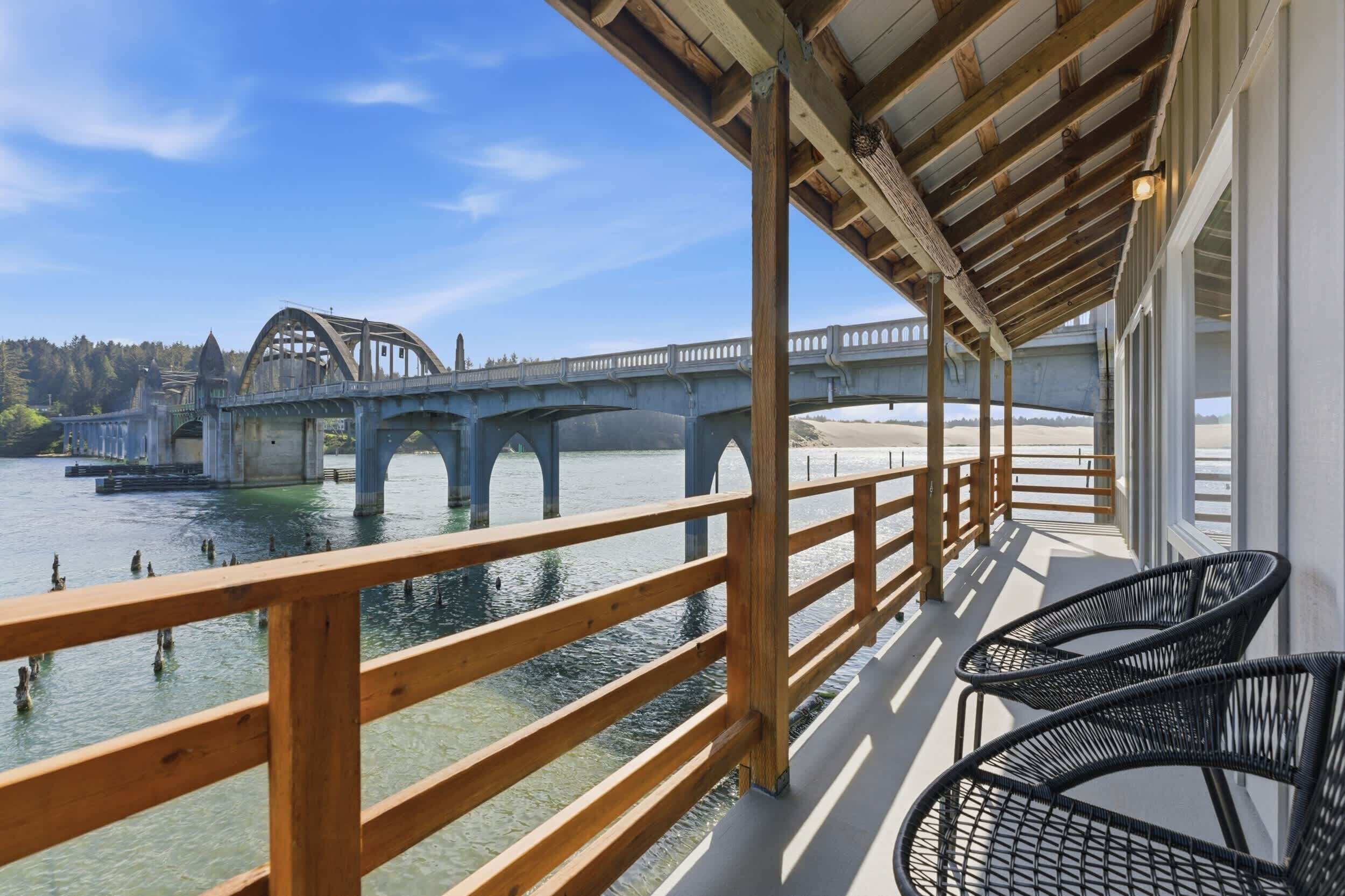 A covered outdoor area with a wooden railing, a view of a bridge, and a body of water.