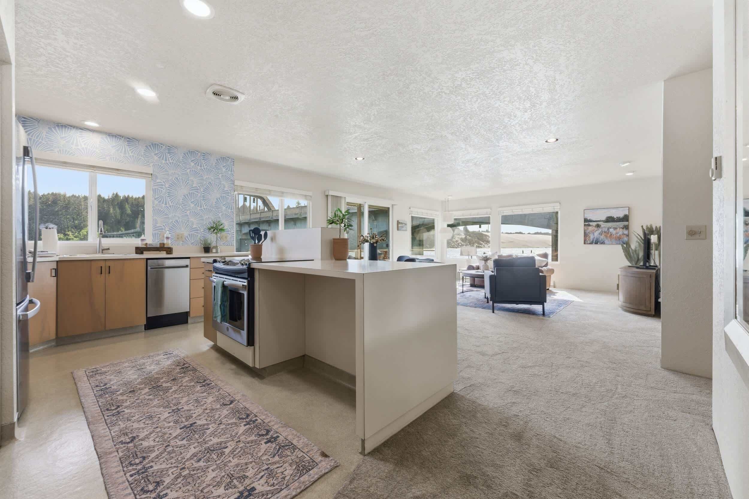 A spacious kitchen with a large island, a dining area with a sofa, and a view of the outdoors through large windows.