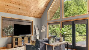 Un salón moderno con televisor grande, asientos cómodos y ventanas amplias que ofrecen vistas a zonas verdes.