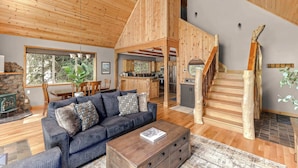 Amplia sala de estar con techo de madera, un sofá, una mesa de centro, una escalera y una zona de cocina.