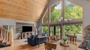 Amplia sala de estar con techo de madera, ventanas grandes, chimenea y una mesa de comedor.