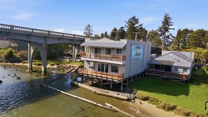 Un bâtiment situé au bord de l’eau, doté d’une terrasse, d’un espace couvert et d’un pont en arrière-plan.