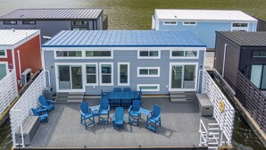 A modern houseboat with a blue roof, a deck with blue chairs, and a view of the water. - Floatopia - A Unique Floating Retreat (Russell Springs)