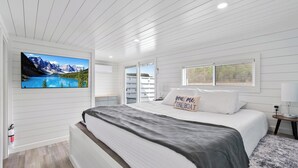 A bedroom with a bed, a mounted TV, a window, and a nightstand. - Floatopia - A Unique Floating Retreat (Russell Springs)