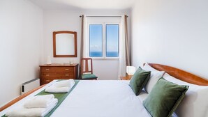 Una habitación de hotel con una cama, un tocador, una silla, un ventanal con vistas y una lámpara.