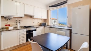 Una cocina compacta con gabinetes blancos, estufa, lavamanos y ventana con vistas.