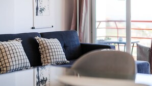 Un sofá azul oscuro con dos almohadones estampados, una obra de arte enmarcada en la pared, y vistas al exterior a través de una ventana.