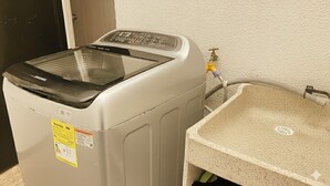 A front-loading washing machine with a control panel, a water inlet hose, and a beige sink with a drain. - Nido del Bosque · Coffee Farm Host · Hot Springs 25 min · Pet Friendly (Dosquebradas)
