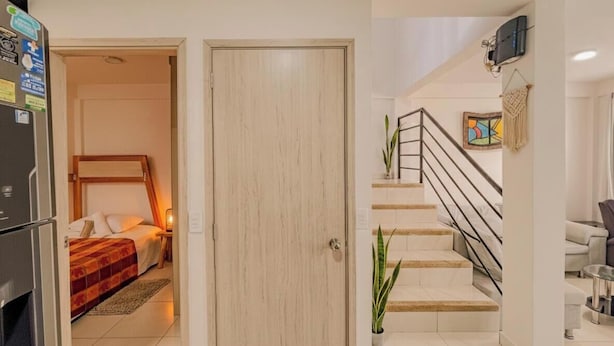 A hotel room with a bed, a nightstand, a refrigerator, a wooden door, a staircase, and a wall-mounted TV. - Nido del Bosque · Coffee Farm Host · Hot Springs 25 min · Pet Friendly (Dosquebradas)