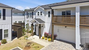 A residential area with multiple houses, a driveway, and a small garden with flowers. - Steps to Beach! Hot Tub, Dogs OK, Pool, Pickleball (Corolla)