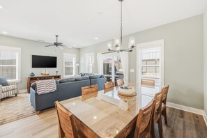 A spacious living room with a large sofa, dining table, and a ceiling fan. - Steps to Beach! Hot Tub, Dogs OK, Pool, Pickleball (Corolla)