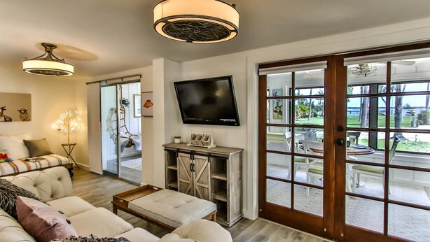 Una sala de estar con sofá, una mesa de centro, televisor y un amplio ventanal corredero que da a un patio exterior.